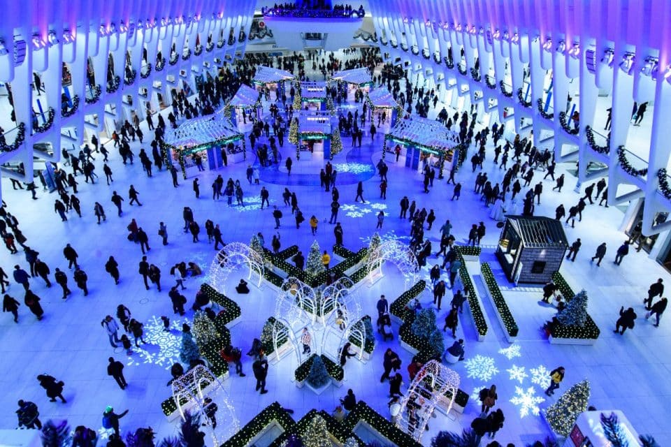 The soaring white ribbed interior hall of the Oculus transit center at the World Trade Center, seen from above with crowds of people crossing the pale floor beneath the skeletal steel arches