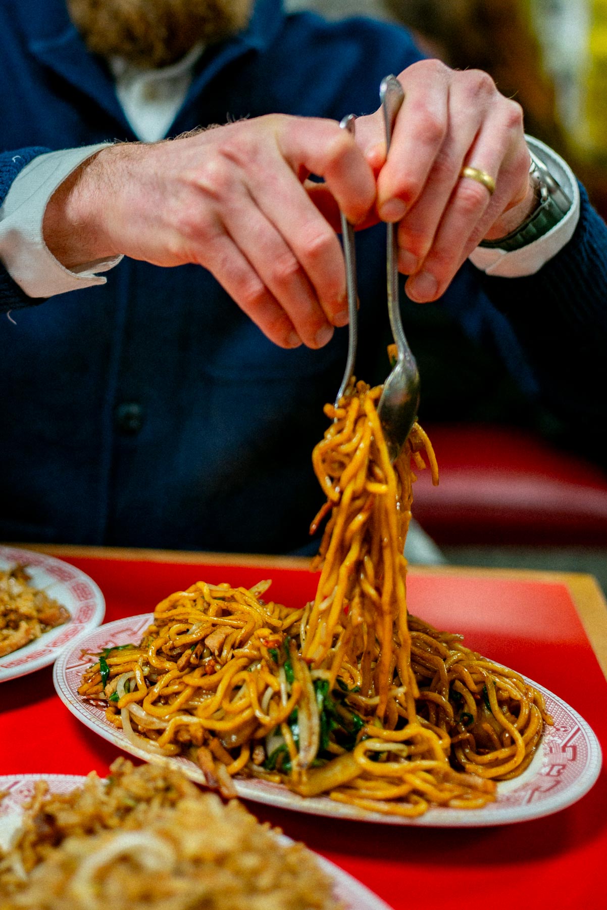 A man helping himself from a plate of noodles from Wo Hop, one of the most famous restaurants in Chinatown NYC