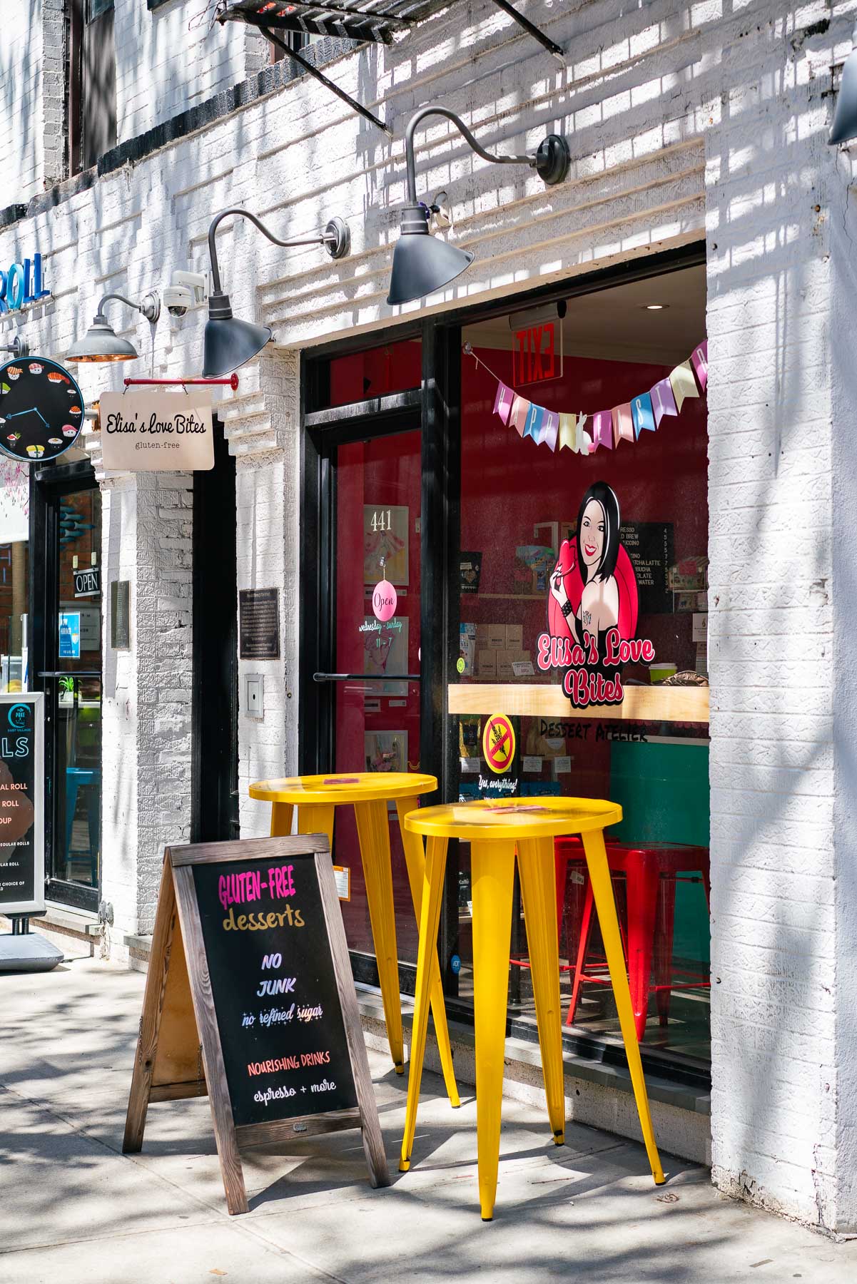 Two yellow metal standing tables at the entrance of Elisa's Love Bites Bakery in the East Village
