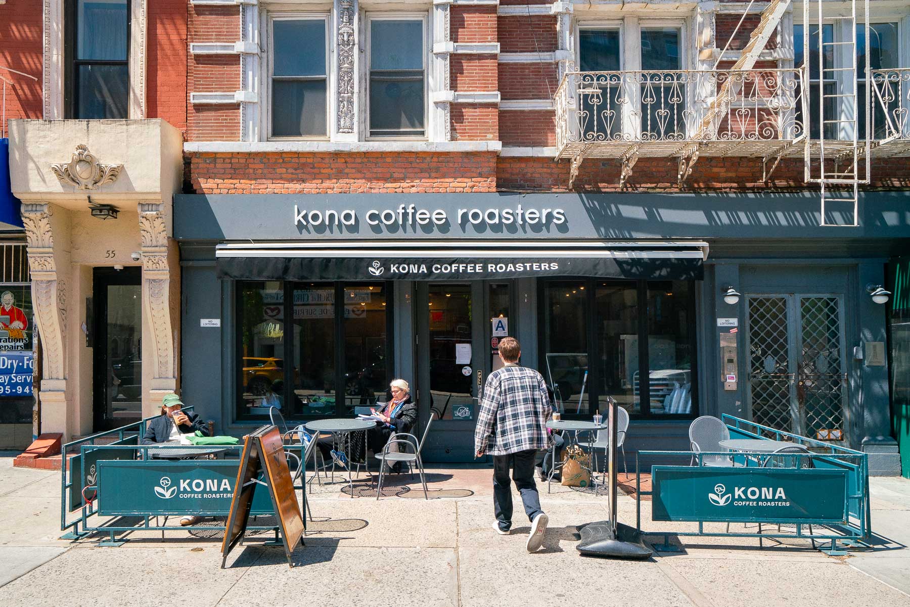Man walking past metal outdoor tables and chairs to the entrance of Kona Coffee Roasters in the East Village