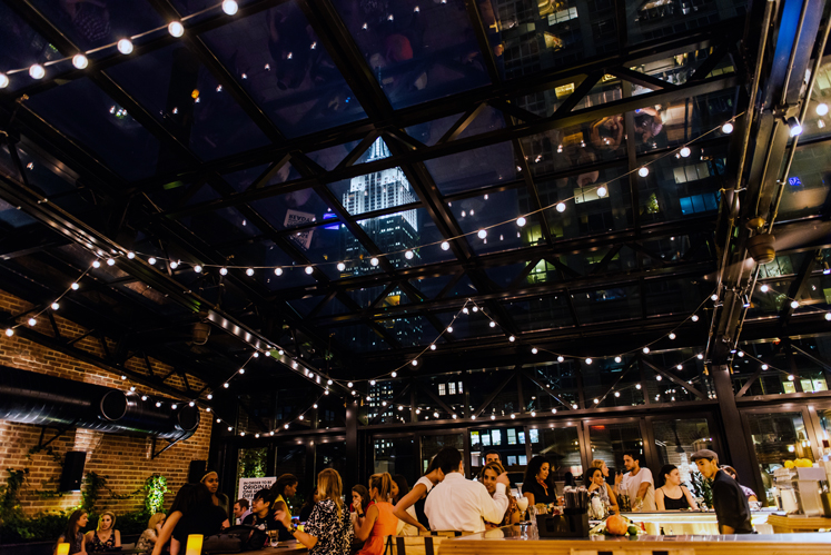 People enjoying drinks under twinkling lights at night in NYC with epic views of the Empire State Building at the Refinery Rooftop bar in Manhattan